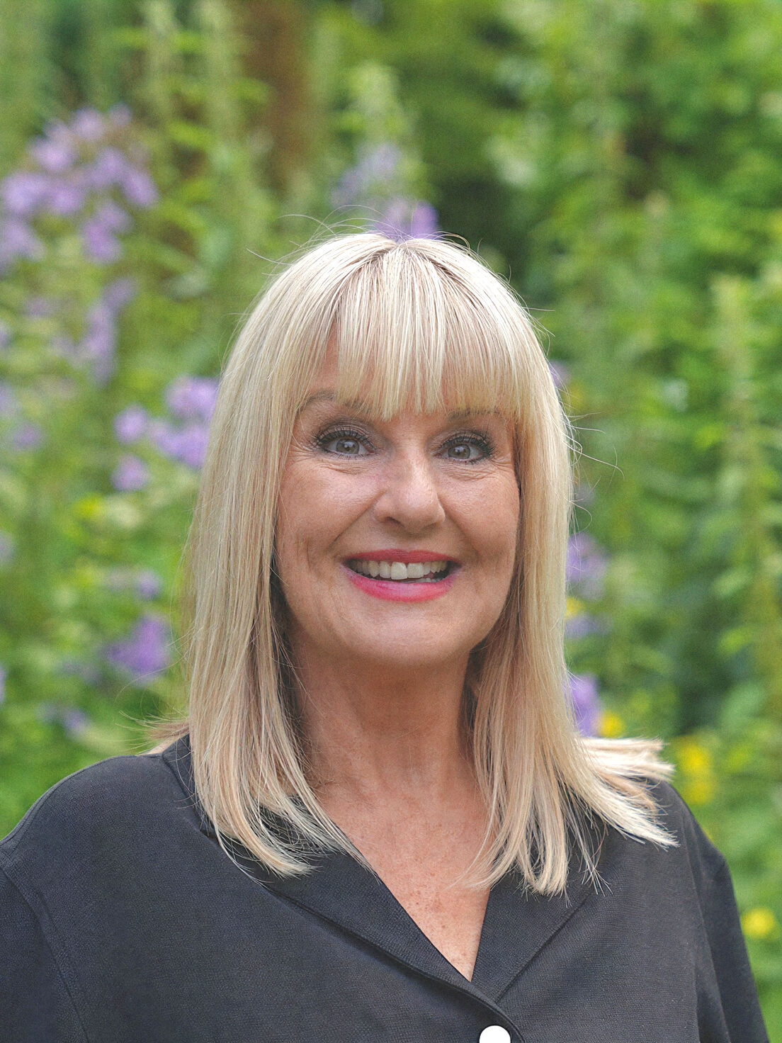 Helen Cassidy, independent celebrant, smiling in a garden of sage greens and soft purple flowers